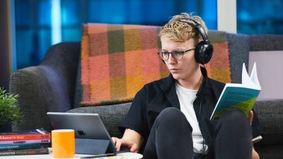 Woman with headphones sitting on floor watching something on iPad whilst holding a book